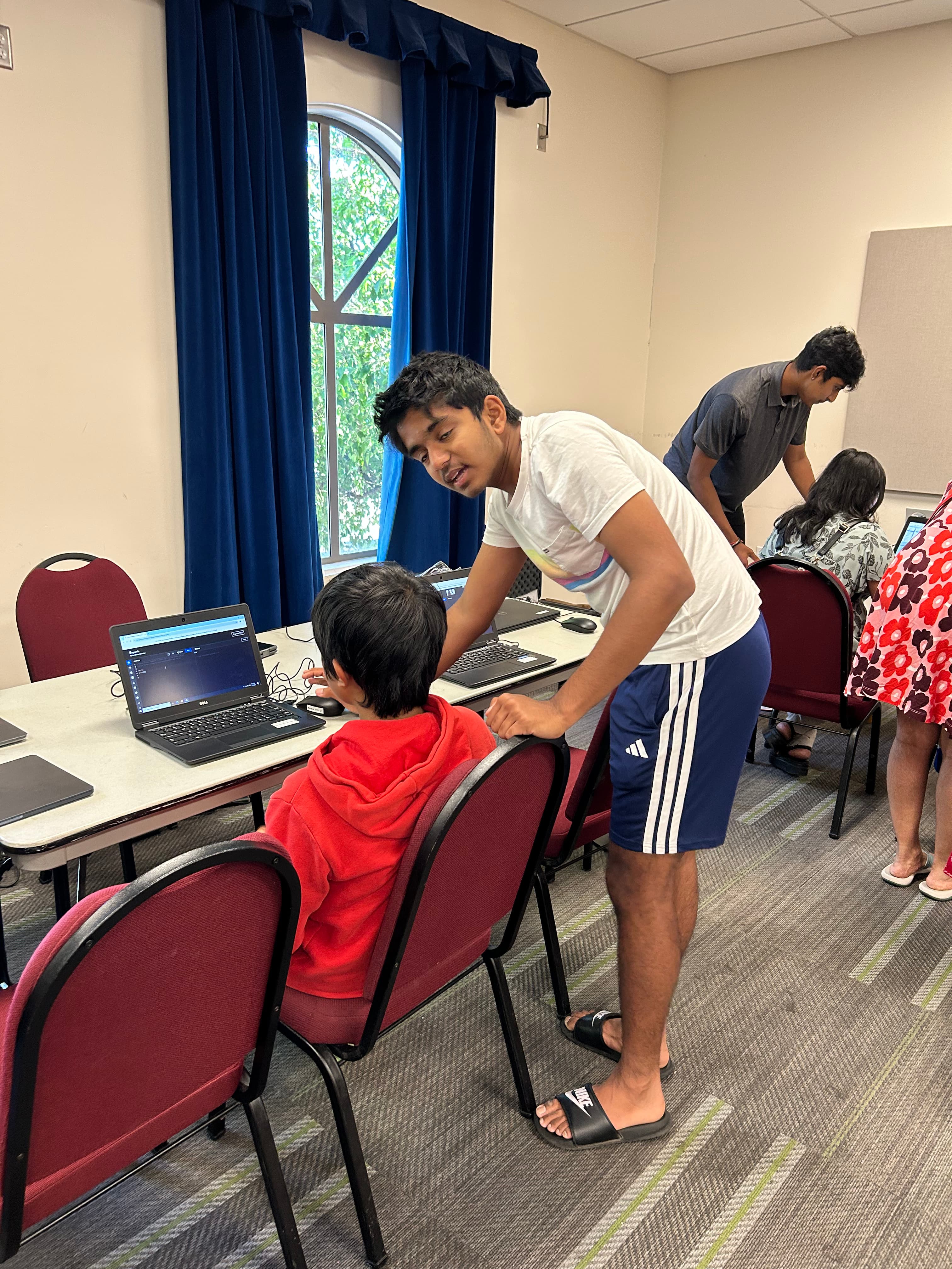 Volunteer leaning in to help a young student at their laptop